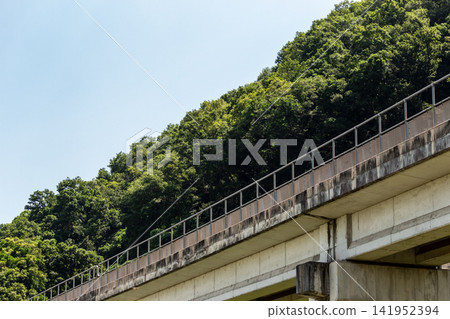A concrete bridge stretching against a backdrop of blue sky and lush green mountains (low angle). A concrete bridge stretching against a backdrop of blue sky and lush green mountains (low angle). 141952394