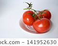 Three red tomatoes on a branch, lying on a white plate on white background 141952630