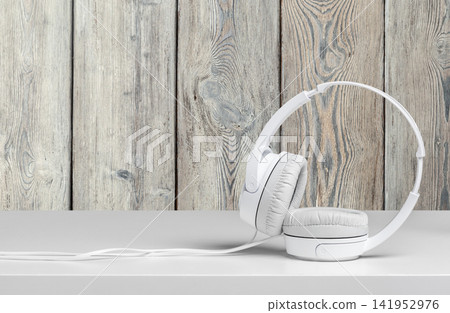 White headphones placed on a table near a wooden wall with a simple design White headphones placed on a table near a wooden wall with a simple design 141952976