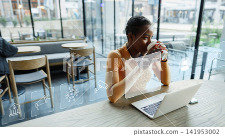 Deep fake technology is explored by a person in a cafe while drinking coffee and using a laptop Deep fake technology is explored by a person in a cafe while drinking coffee and using a laptop 141953002