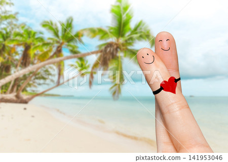 Fingers with faces holding a heart decoration on a beach with palm trees and water Fingers with faces holding a heart decoration on a beach with palm trees and water 141953046
