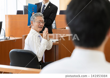 A young prosecutor explains to a senior male witness who is testifying in court, showing evidence. A young prosecutor explains to a senior male witness who is testifying in court, showing evidence. 141953084
