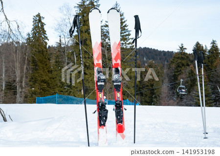 Ski gear positioned upright in snow with mountains in background Ski gear positioned upright in snow with mountains in background 141953198