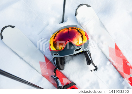 Ski goggles and poles rest on snowy terrain alongside skis Ski goggles and poles rest on snowy terrain alongside skis 141953200