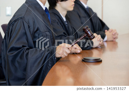 Close-up of a judge's hands striking a wooden mallet in court. Close-up of a judge's hands striking a wooden mallet in court. 141953327