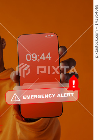 Emergency alert on phone held by person with plain background shows time and notification symbol Emergency alert on phone held by person with plain background shows time and notification symbol 141954069