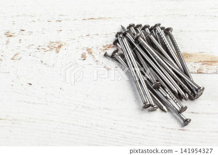 Pile of metal nails lying on white wooden surface Pile of metal nails lying on white wooden surface 141954327