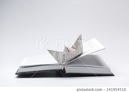 Paper boat sits on open book, pages with writing shown 141954518
