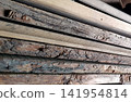 A close-up photograph capturing a stack of raw wooden planks. The image highlights the dynamic contrast between rough, natural bark-covered edges and the smooth, milled faces of the lumber 141954814