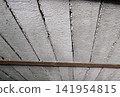 Detailed bottom-up perspective of rough, precast concrete beams forming ceiling structure. Notice the jagged dark seams between slabs, horizontal rusty metal support bar crossing the lower section. 141954815
