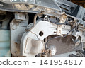Detailed close-up shot revealing the exposed front structure of a car. The bumper cover is removed, showing the frame rail, radiator, wiring, brackets, bolts, small horn, an LED work light accessory. 141954817