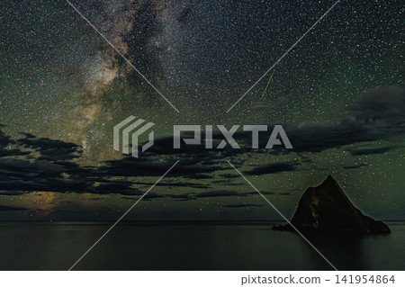 The surreal rock formation, Madoiwa, stands majestically in the darkness, dramatically illuminating the night sky with the Milky Way galaxy and a spectacular display of shooting stars. The surreal rock formation, Madoiwa, stands majestically in the darkness, dramatically illuminating the night sky with the Milky Way galaxy and a spectacular display of shooting stars. 141954864