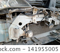 A dusty, detailed view of a car's front engine bay. Components like the radiator, part of a headlight, extensive wiring harnesses, a horn, and an auxiliary LED light are visible. 141955005