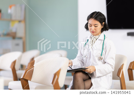 Young woman in medical coat taking notes on tablet in lecture hall Young woman in medical coat taking notes on tablet in lecture hall 141955041