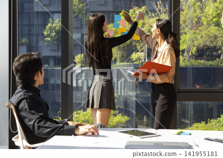Two business woman presenting working project on the window of office building. Business, people, teamwork and planning concept. Two business woman presenting working project on the window of office building. Business, people, teamwork and planning concept. 141955181