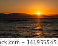 Sunrise over the Red Sea in Dahab, Egypt. The sun rises above the horizon, illuminating the water. Mountains of Saudi Arabia are visible in the background. 141955545