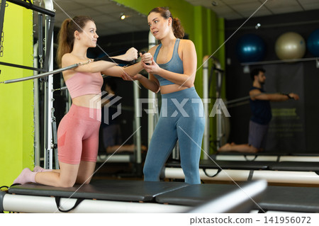 Female trainer guiding girl during arm strength workout on reformer Female trainer guiding girl during arm strength workout on reformer 141956072