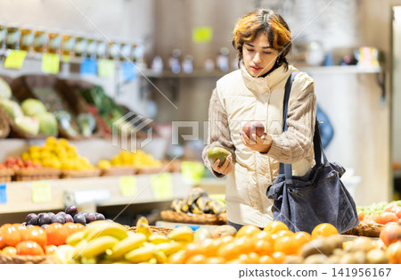 Girl near vegetable stand in store choose mango. Girl near vegetable stand in store choose mango. 141956167