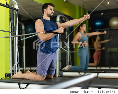 Young man training arms and shoulders on pilates reformer Young man training arms and shoulders on pilates reformer 141956174