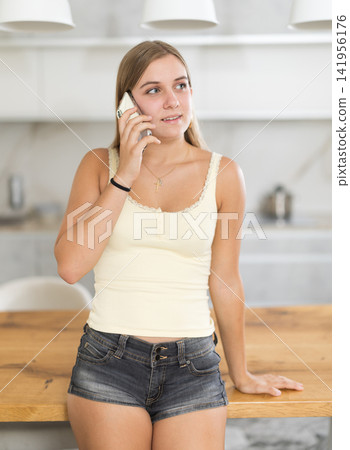 Teenage girl talking on mobile phone in her kitchen at home Teenage girl talking on mobile phone in her kitchen at home 141956176