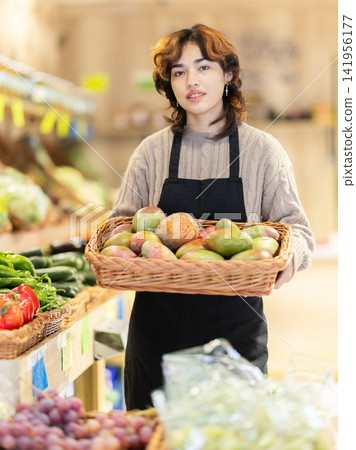 Woman employees in uniform carries wicker basket with mango in grocery shop Woman employees in uniform carries wicker basket with mango in grocery shop 141956177
