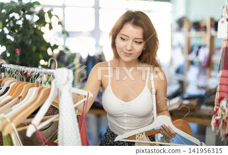 Young woman chooses dresses and tops in store Young woman chooses dresses and tops in store 141956315