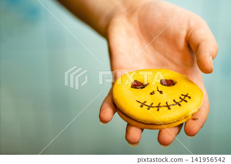 Hand holding a decorated Halloween pumpkin cookie close up Hand holding a decorated Halloween pumpkin cookie close up 141956542