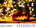 Spooky Halloween pumpkin lantern sitting on a table with warm bokeh background 141956578