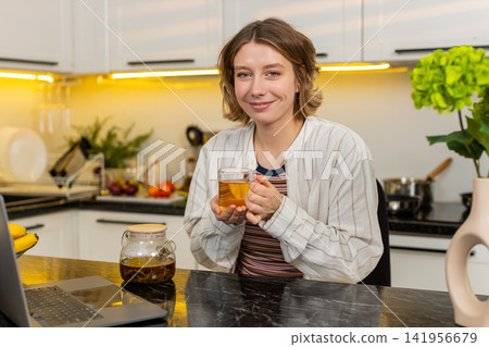 Young woman drinking hot herbal tea in home kitchen enjoying calm diet break and cozy healthy rest Young woman drinking hot herbal tea in home kitchen enjoying calm diet break and cozy healthy rest 141956679