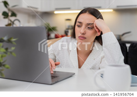 Young woman bored writes in notebook works on laptop low drive demotivated burnout focus fatigue Young woman bored writes in notebook works on laptop low drive demotivated burnout focus fatigue 141956704