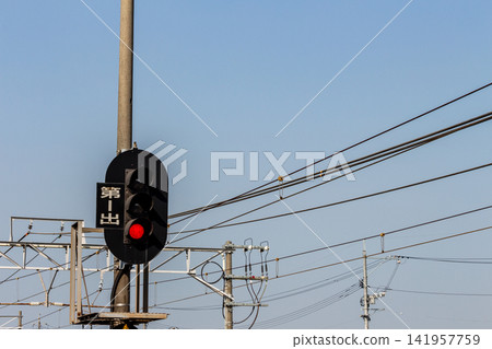 A railway departure signal and overhead wires with a red (stop) signal lit against a blue sky. A railway departure signal and overhead wires with a red (stop) signal lit against a blue sky. 141957759
