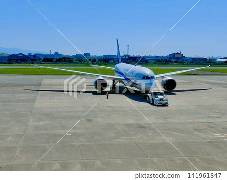 An ANA passenger plane being towed by a towing vehicle against the blue sky of the airport. An ANA passenger plane being towed by a towing vehicle against the blue sky of the airport. 141961847