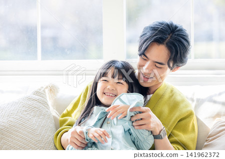 A smiling daughter sitting on her father's lap. A smiling daughter sitting on her father's lap. 141962372