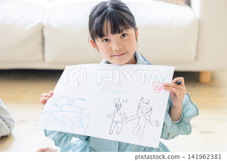 A smiling girl happily shows off a picture of her family that she drew herself. A smiling girl happily shows off a picture of her family that she drew herself. 141962381