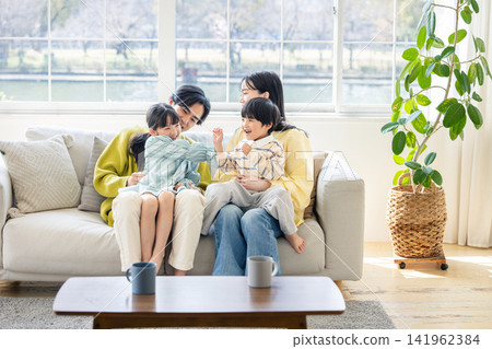 A family of four happily chatting on the sofa in their sunny living room. A family of four happily chatting on the sofa in their sunny living room. 141962384