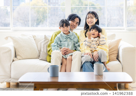 A family of four happily snuggling together in the living room, smiling. A family of four happily snuggling together in the living room, smiling. 141962388