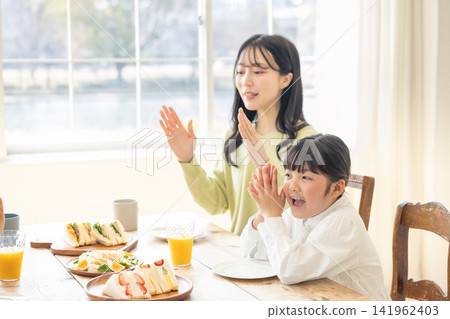 一位母親和她的女兒雙手合十,說“Itadakimasu”(謝謝你們的款待)。 一位母親和她的女兒雙手合十,說“Itadakimasu”(謝謝你們的款待)。 141962403