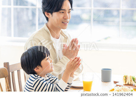 A father puts his hands together and says "thank you for the meal" with his son. A father puts his hands together and says "thank you for the meal" with his son. 141962404