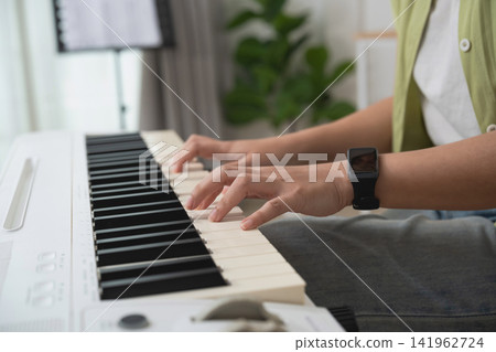 Person Playing Keyboard Piano in Modern Living Room with Green Plants and Natural Lighting Person Playing Keyboard Piano in Modern Living Room with Green Plants and Natural Lighting 141962724