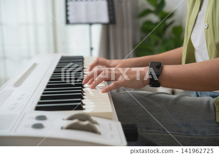Person Playing Piano Keyboard at Home with Digital Device on Wrist Watch and Natural Light from Window Person Playing Piano Keyboard at Home with Digital Device on Wrist Watch and Natural Light from Window 141962725