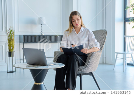 Young female specialist writing in notepad during work in modern office space Young female specialist writing in notepad during work in modern office space 141963145