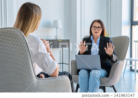 Professional female psychologist with laptop consulting young woman in modern clinic Professional female psychologist with laptop consulting young woman in modern clinic 141963147