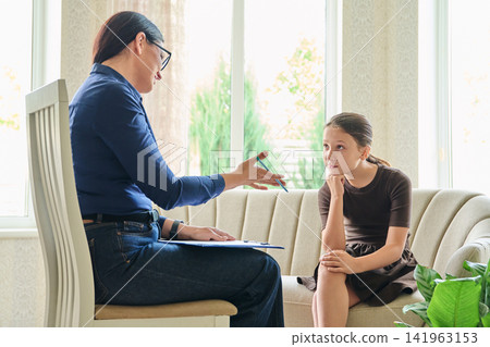 Female psychologist talking to a young girl during a therapy consultation Female psychologist talking to a young girl during a therapy consultation 141963153