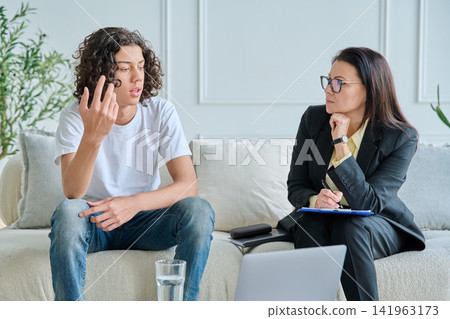 Psychologist listening to teenage boy in office Psychologist listening to teenage boy in office 141963173