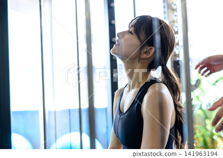 一位女士坐在史密斯機上,調整呼吸,接受健身房教練的指導。早晨染髮。 一位女士坐在史密斯機上,調整呼吸,接受健身房教練的指導。早晨染髮。 141963194