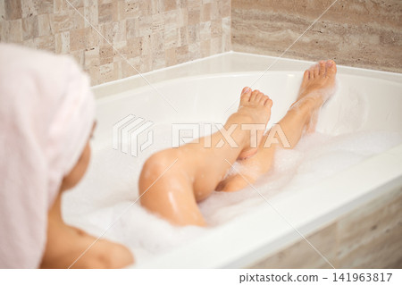 Woman soaking legs in a warm bubble bath, experiencing deep relaxation and personal self-care moment at home Woman soaking legs in a warm bubble bath, experiencing deep relaxation and personal self-care moment at home 141963817