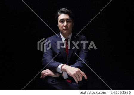 Portrait of a businessman in his 30s, in darkness, looking directly at the camera. Portrait of a businessman in his 30s, in darkness, looking directly at the camera. 141963850