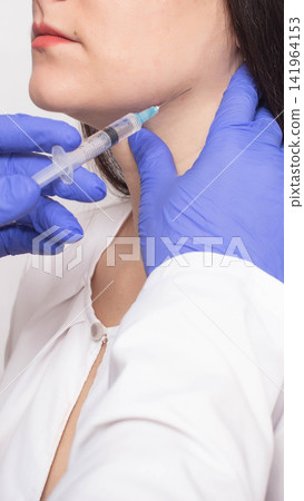 Close-up of woman receiving cosmetic injection in neck area from medical professional hand wearing blue glove holding syringe in medical setting vertical photo, beauty injections Close-up of woman receiving cosmetic injection in neck area from medical professional hand wearing blue glove holding syringe in medical setting vertical photo, beauty injections 141964153