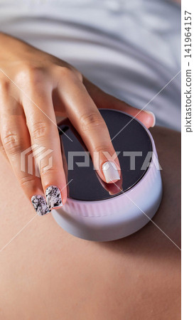 Close up view of person hand holding round portable beauty device for skin treatment against light skin background with focus on manicure and technology application vertical photo, anti-cellulite Close up view of person hand holding round portable beauty device for skin treatment against light skin background with focus on manicure and technology application vertical photo, anti-cellulite 141964157