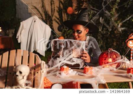 Child dressed as witch holding lantern on Halloween night 141964169